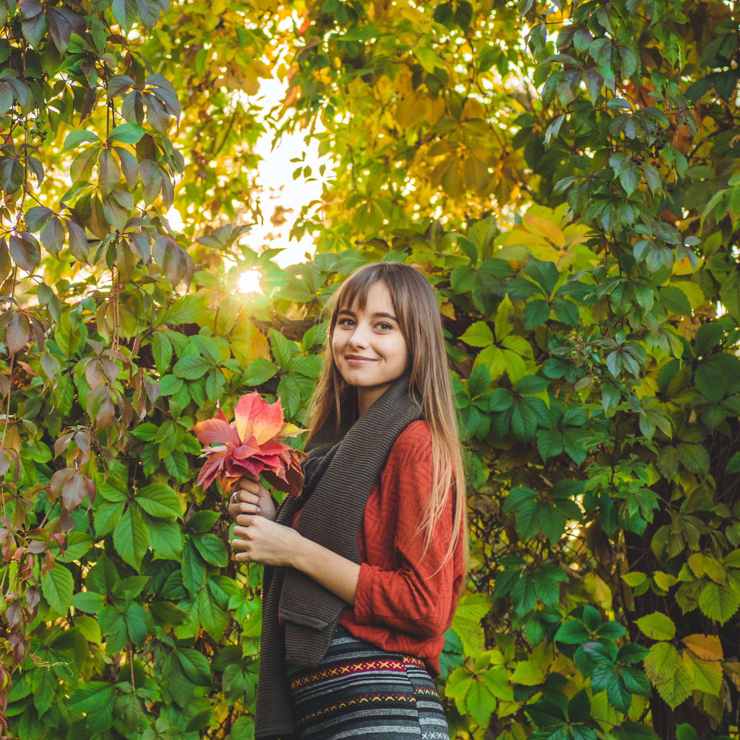 Beauty Romantic Girl Outdoors enjoying nature holding leaves in hands. Beautiful autumn model with waving glow hair. Sun light on sunset. Portrait of romantic female